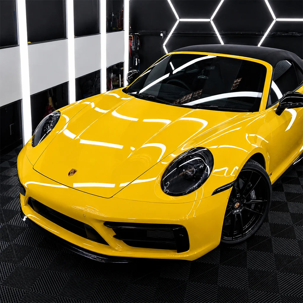 Yellow Porsche 911 convertible with paint protection film displayed in a modern vehicle detailing studio