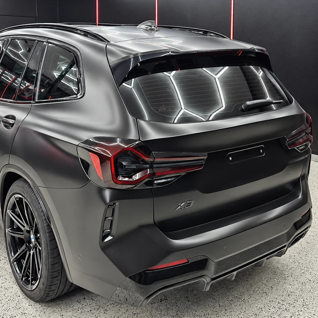 Rear three-quarter view of a BMW X3 featuring a satin black vehicle wrap and gloss black accents in a detailing studio