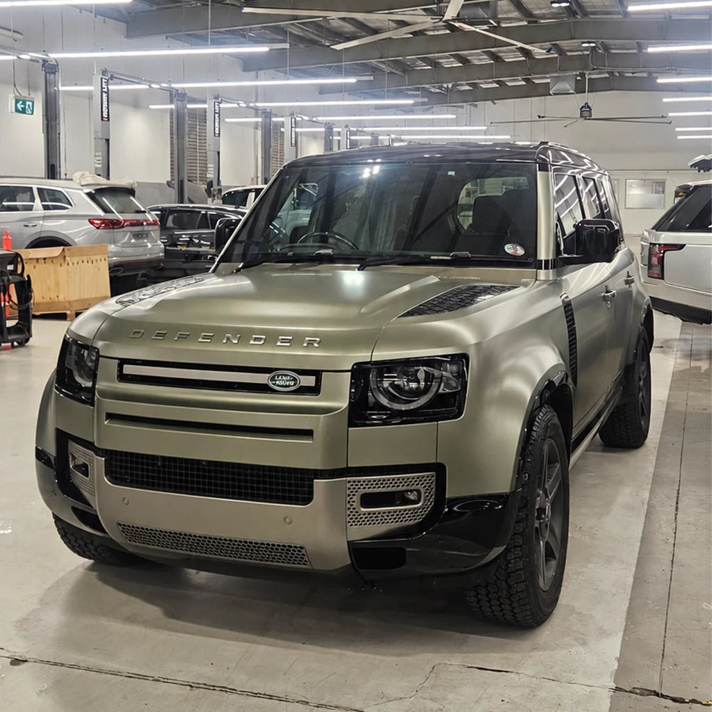 Land Rover Defender featuring a satin olive-green vehicle wrap and contrasting black accents inside a workshop