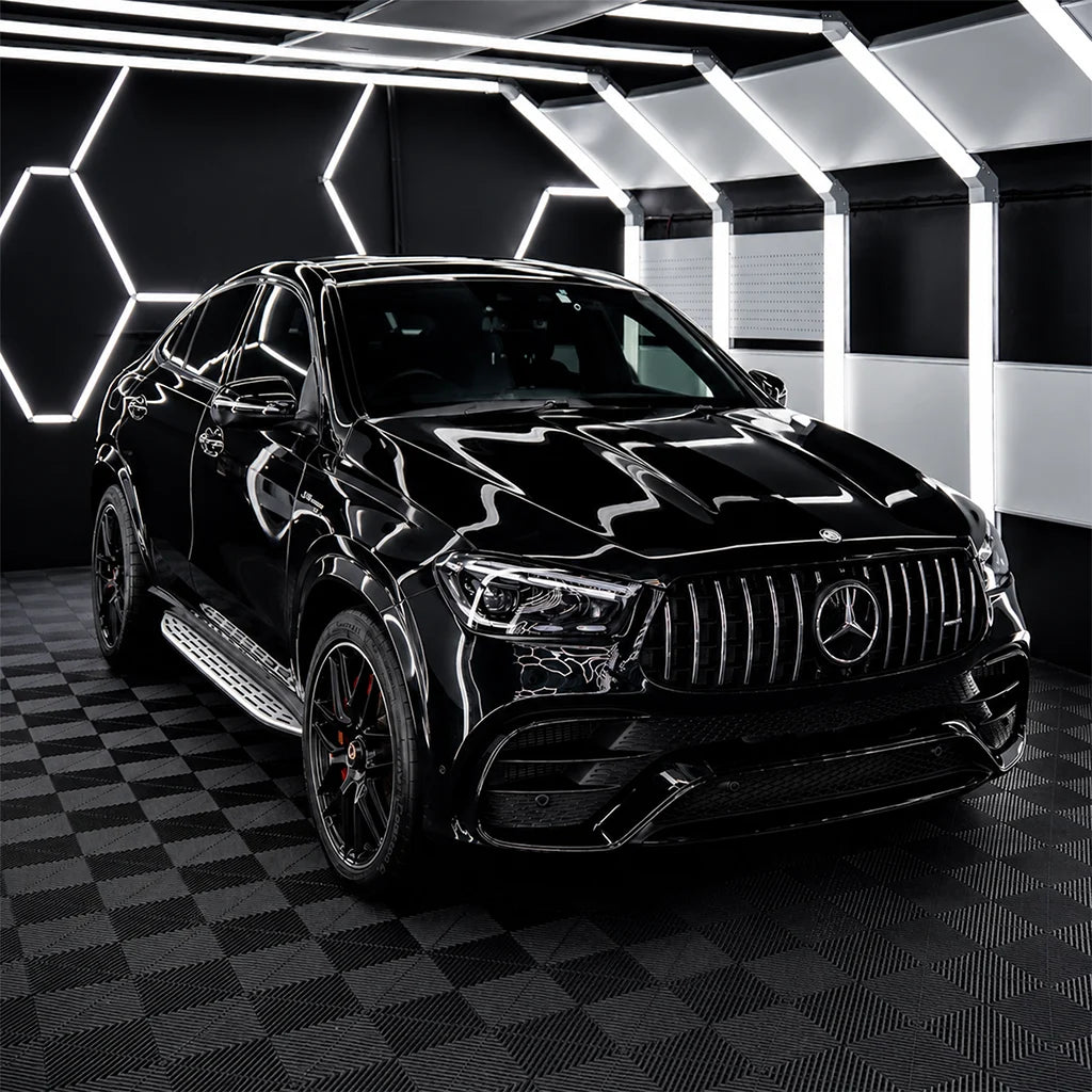 Glossy black Mercedes-AMG SUV displayed inside a premium automotive workshop with geometric lighting